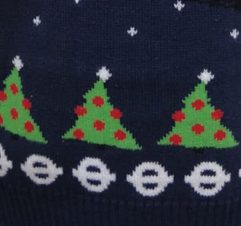 Small proportion of Christmas jumper design showing green Christmas tress on a navy background with white roundels underneath 